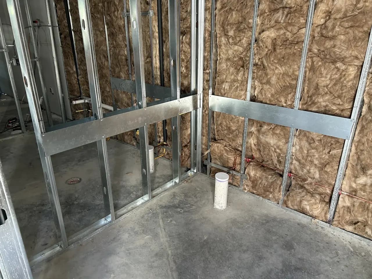 Metal stud framing, insulation and floor-level pipe within the Consumer Cellular Fort Myers tenant space