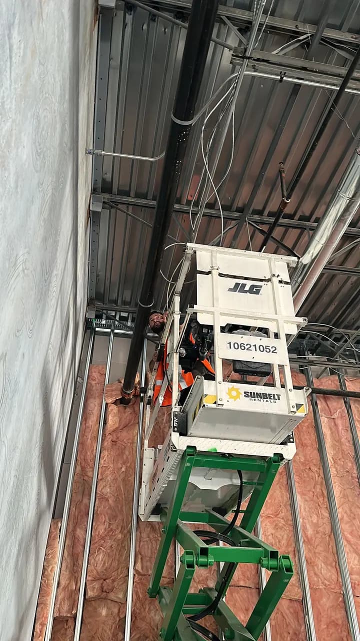 Project worker on a scissor lift beside insulated framing and exposed ceiling structure at Consumer Cellular Fort Myers